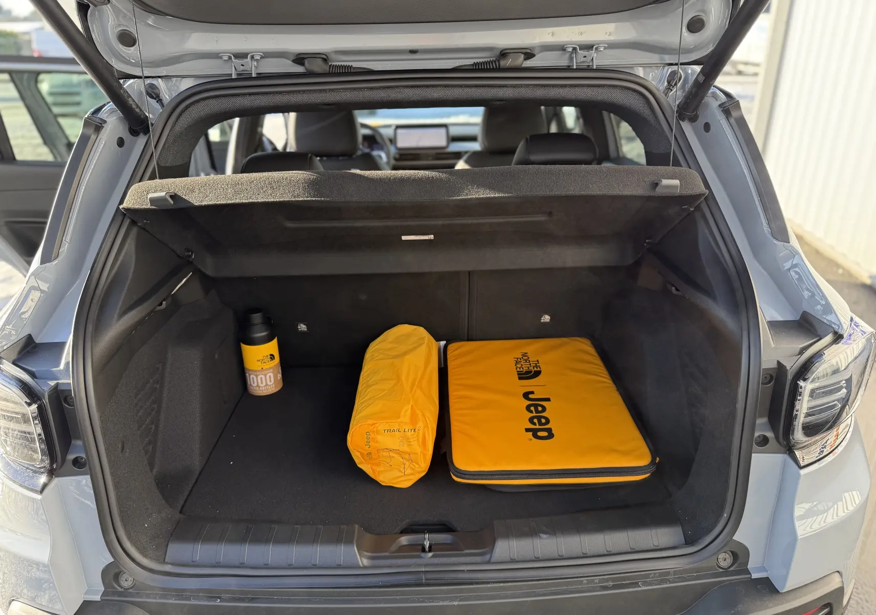 Vue arrière du coffre ouvert du Jeep Avenger Storm Grey 2025, avec accessoires jaunes The North Face visibles à l'intérieur.