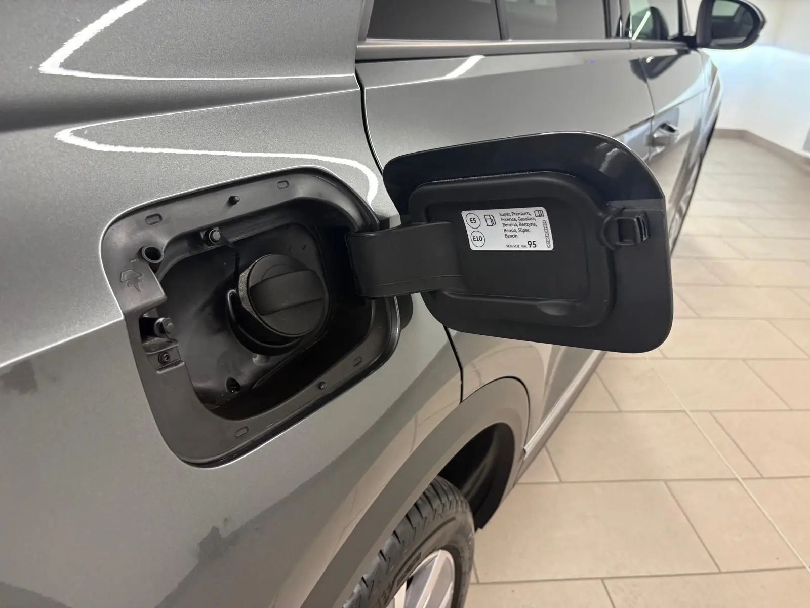 Vue rapprochée de la trappe à carburant ouverte côté gauche d’un Volkswagen T-Roc gris Indium 2025.
