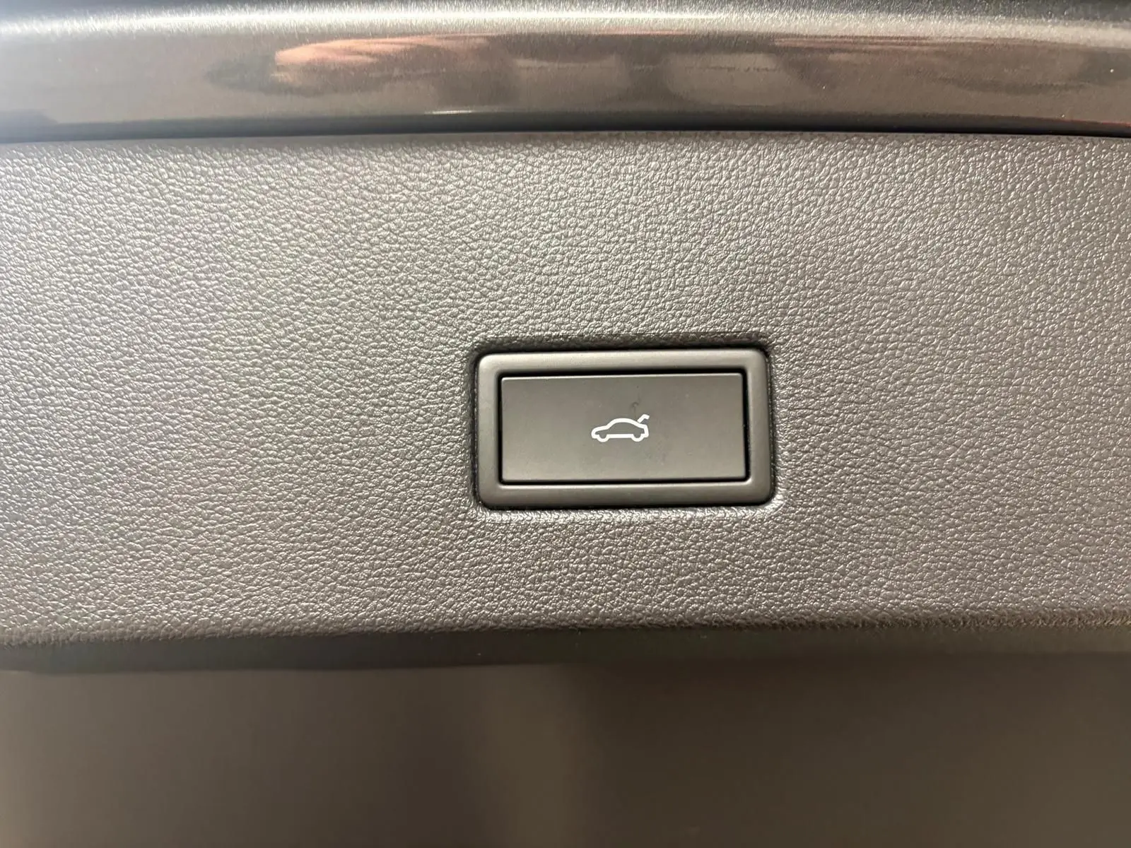 Bouton d'ouverture électrique du coffre sur la garniture intérieure d'un Volkswagen T-Roc Gris Indium 2025.