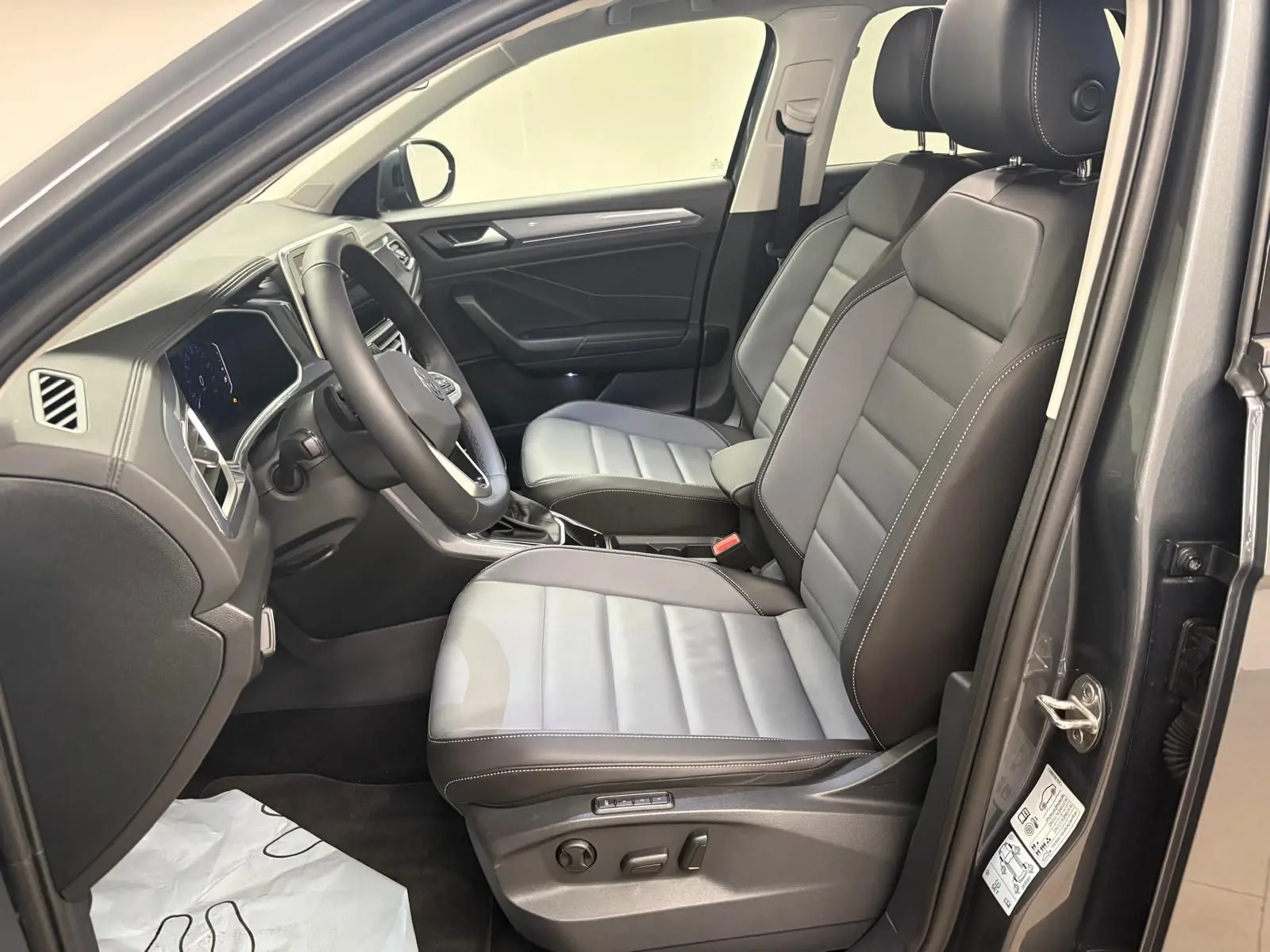 Vue intérieure côté conducteur du Volkswagen T-Roc 2025 avec sièges bi-ton gris et noir, volant multifonctions et tableau de bord moderne.
