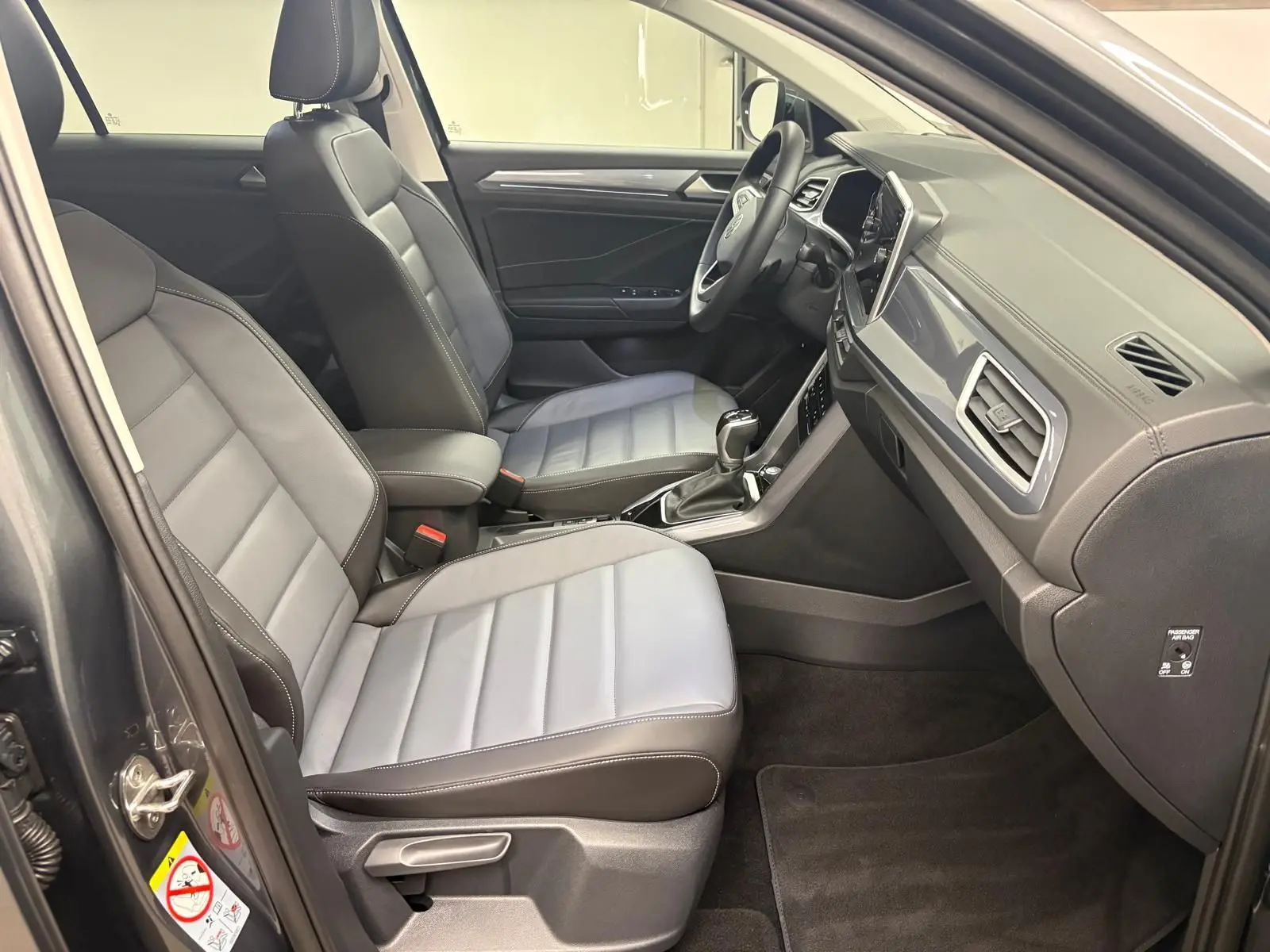 Intérieur avant du Volkswagen T-Roc 2025 en gris Indium, vue côté conducteur avec sièges en cuir et tableau de bord moderne.