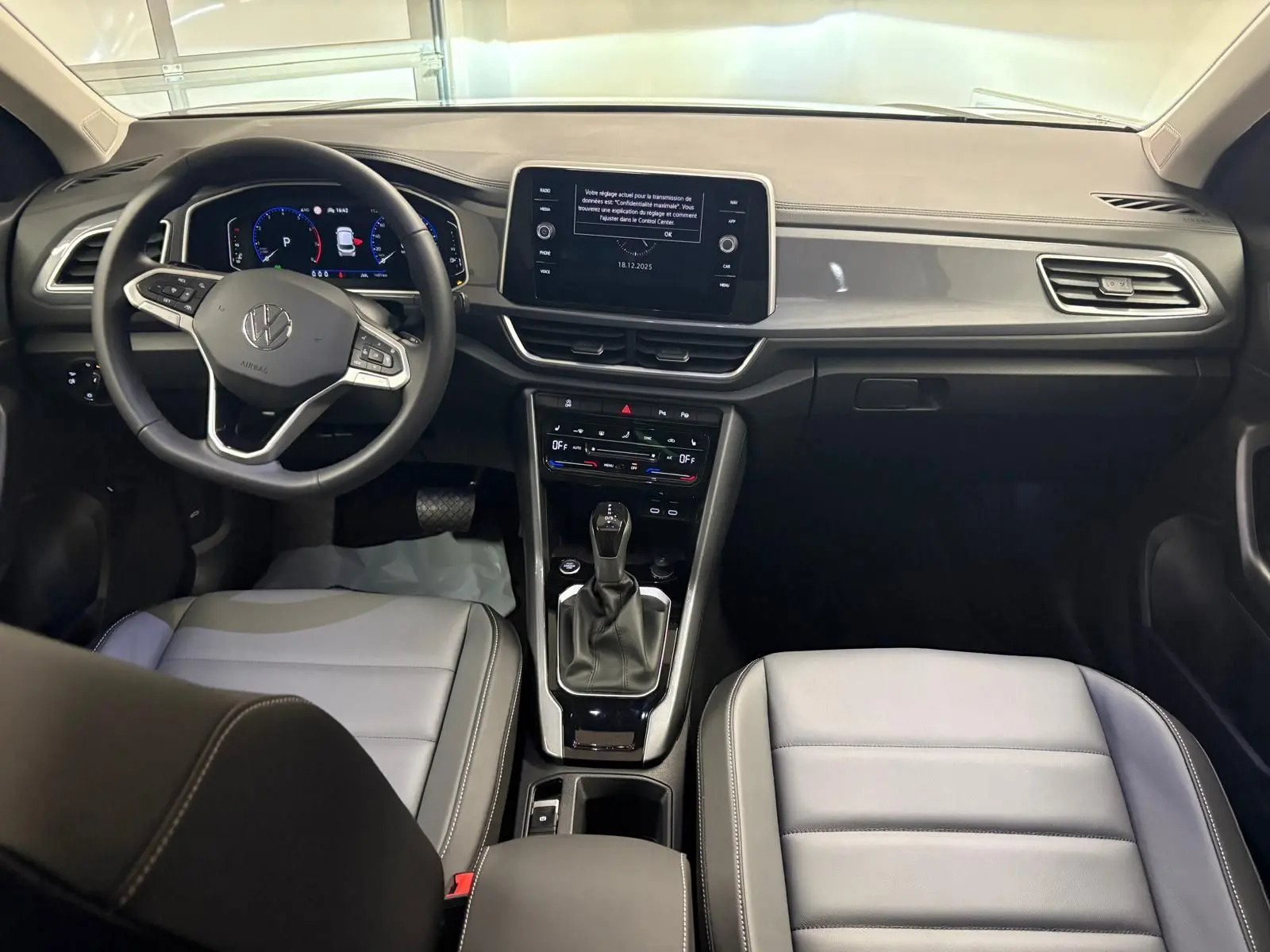 Vue intérieure avant du Volkswagen T-Roc 2025, tableau de bord moderne avec écran central et sièges gris clair.