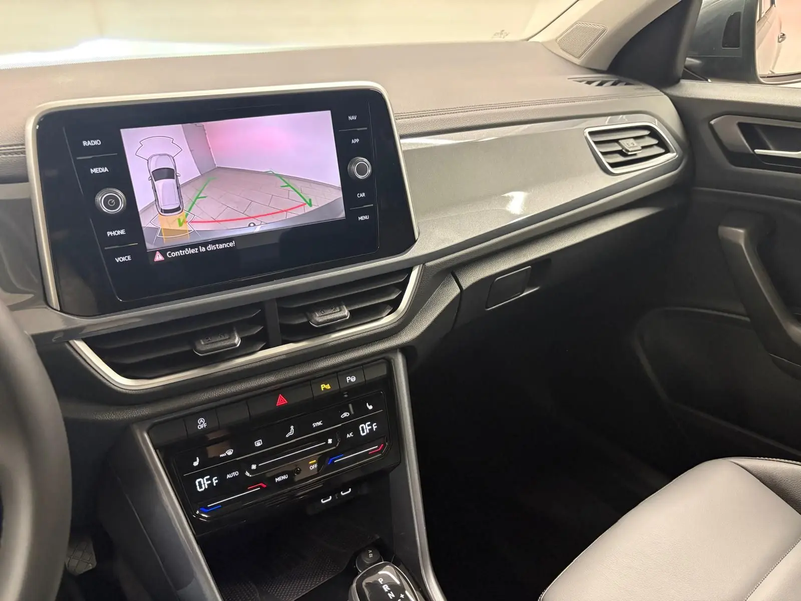 Vue intérieure côté passager du tableau de bord du Volkswagen T-Roc 2025, avec écran tactile et commandes climatisation visibles.