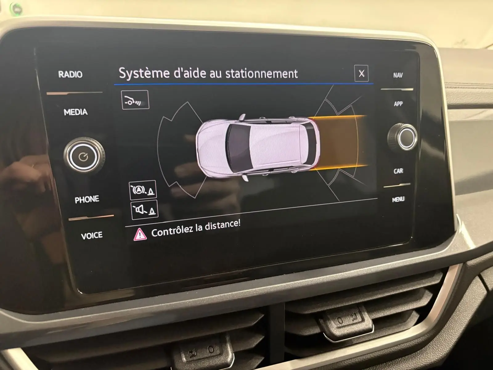 Écran tactile du système d'aide au stationnement du Volkswagen T-Roc 2025 montrant une vue aérienne du véhicule gris Indium.