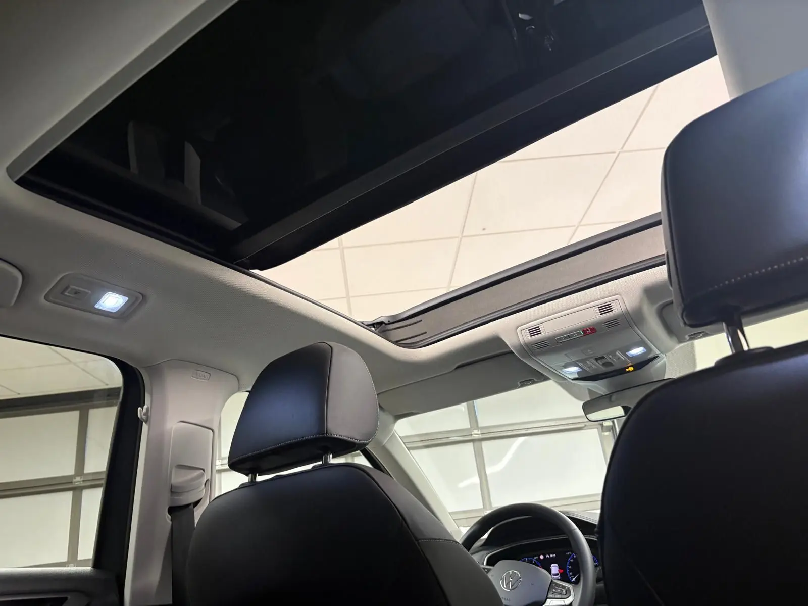 Vue intérieure du Volkswagen T-Roc 2025 montrant le toit ouvrant panoramique et les appuie-têtes avant en cuir noir.