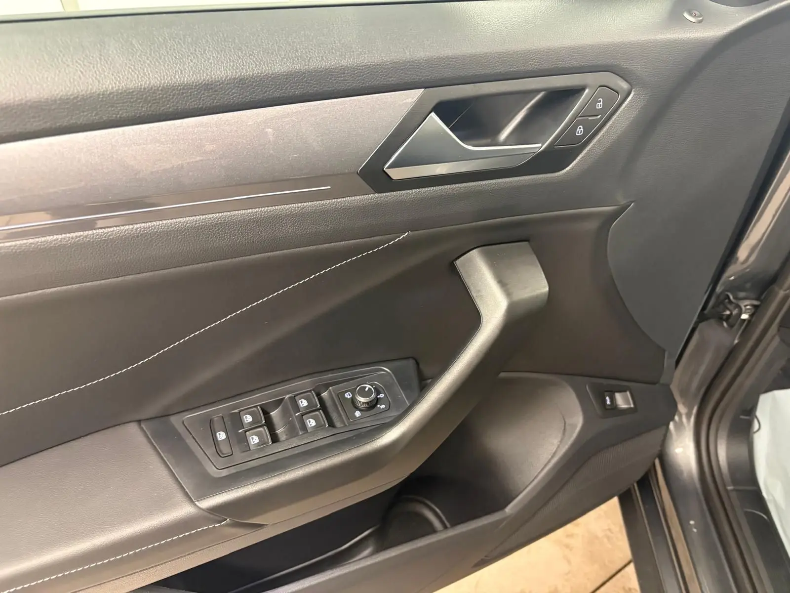 Gros plan sur la porte avant gauche du Volkswagen T-Roc gris Indium, montrant les commandes des vitres et la poignée intérieure.