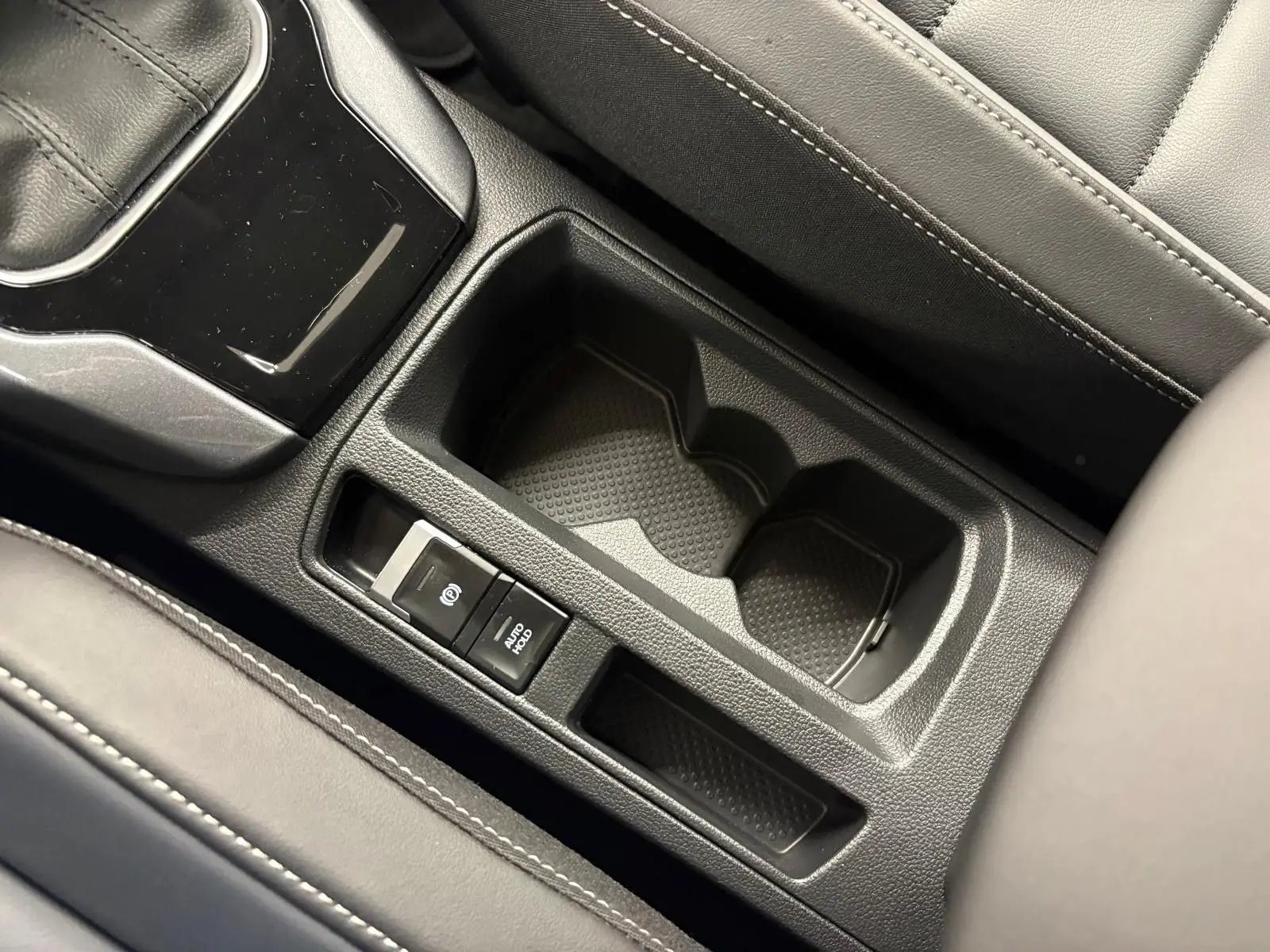 Gros plan sur la console centrale noire du Volkswagen T-Roc 2025 avec porte-gobelets et frein à main électronique.