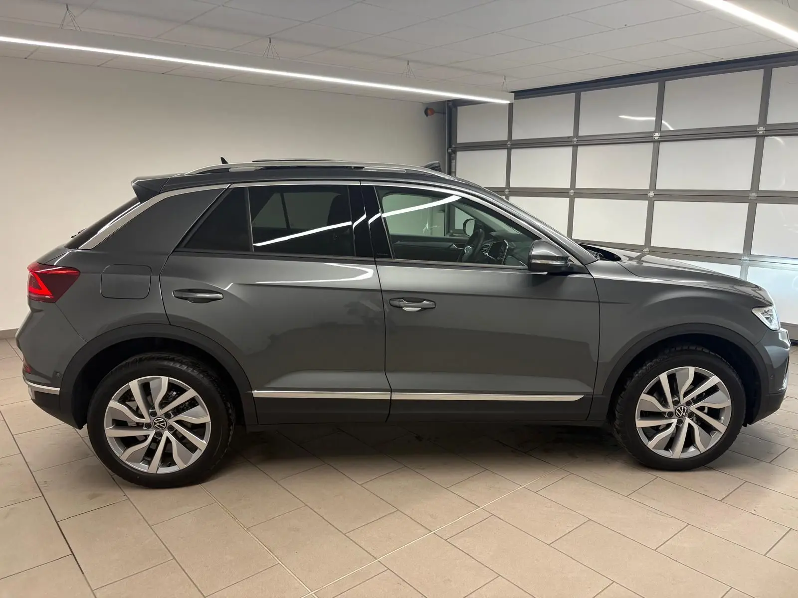 Volkswagen T-Roc 2025 gris Indium vu de profil côté gauche, avec attelage amovible visible à l'arrière.
