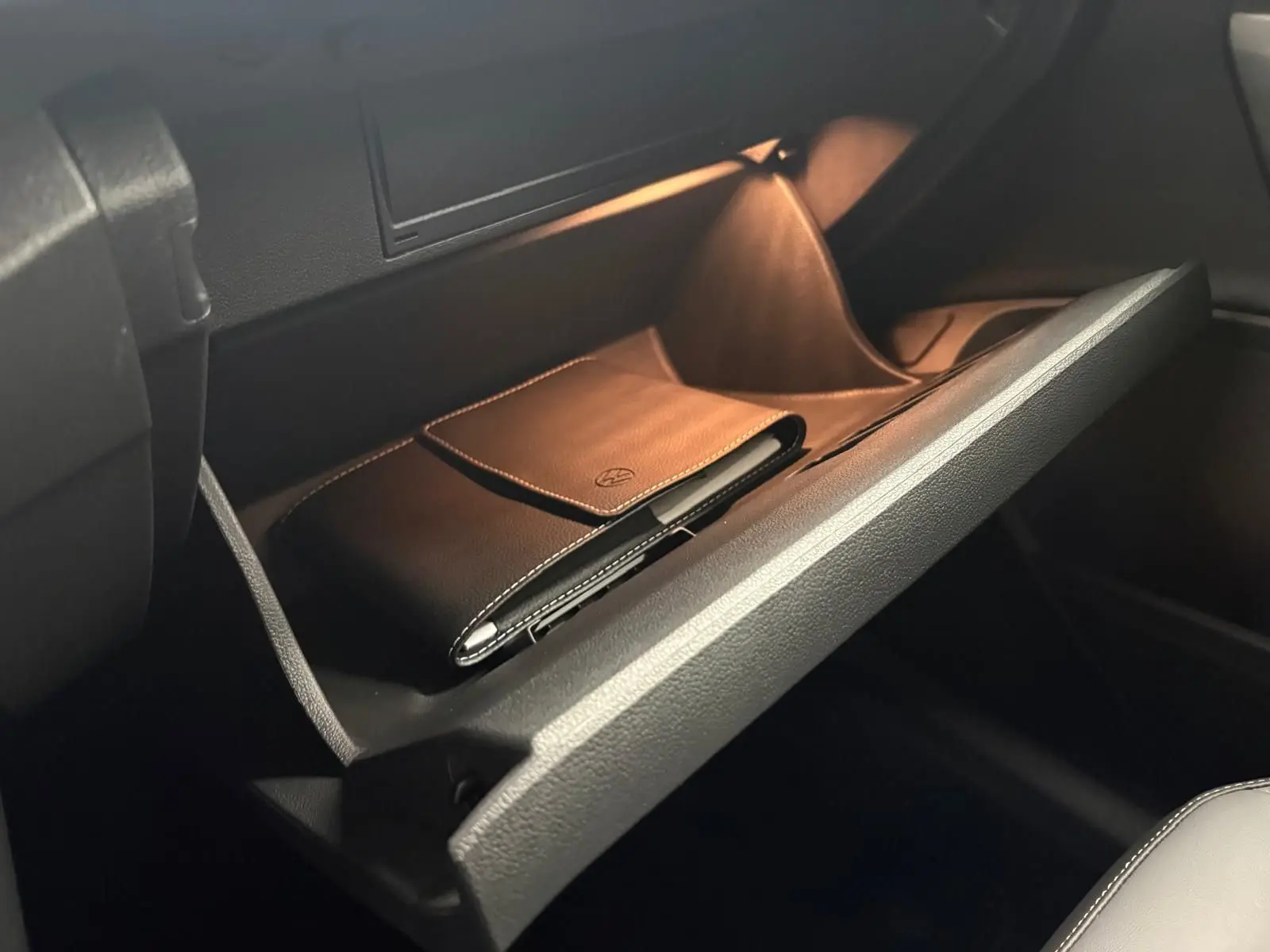 Gant de boîte à gants ouvert avec pochette en cuir noir marqué Volkswagen, intérieur sombre du Volkswagen T-Roc.