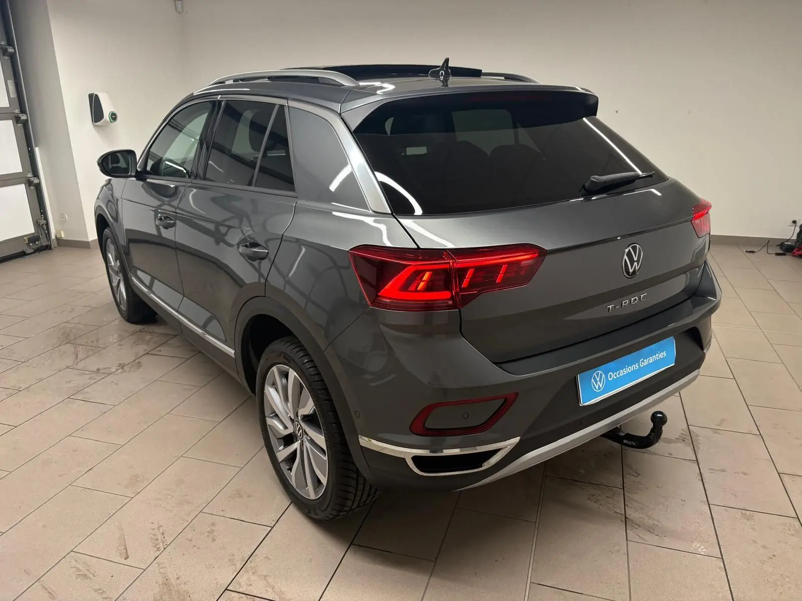 Volkswagen T-Roc 2025 gris Indium vu en 3/4 arrière droit avec attelage amovible dans un garage.