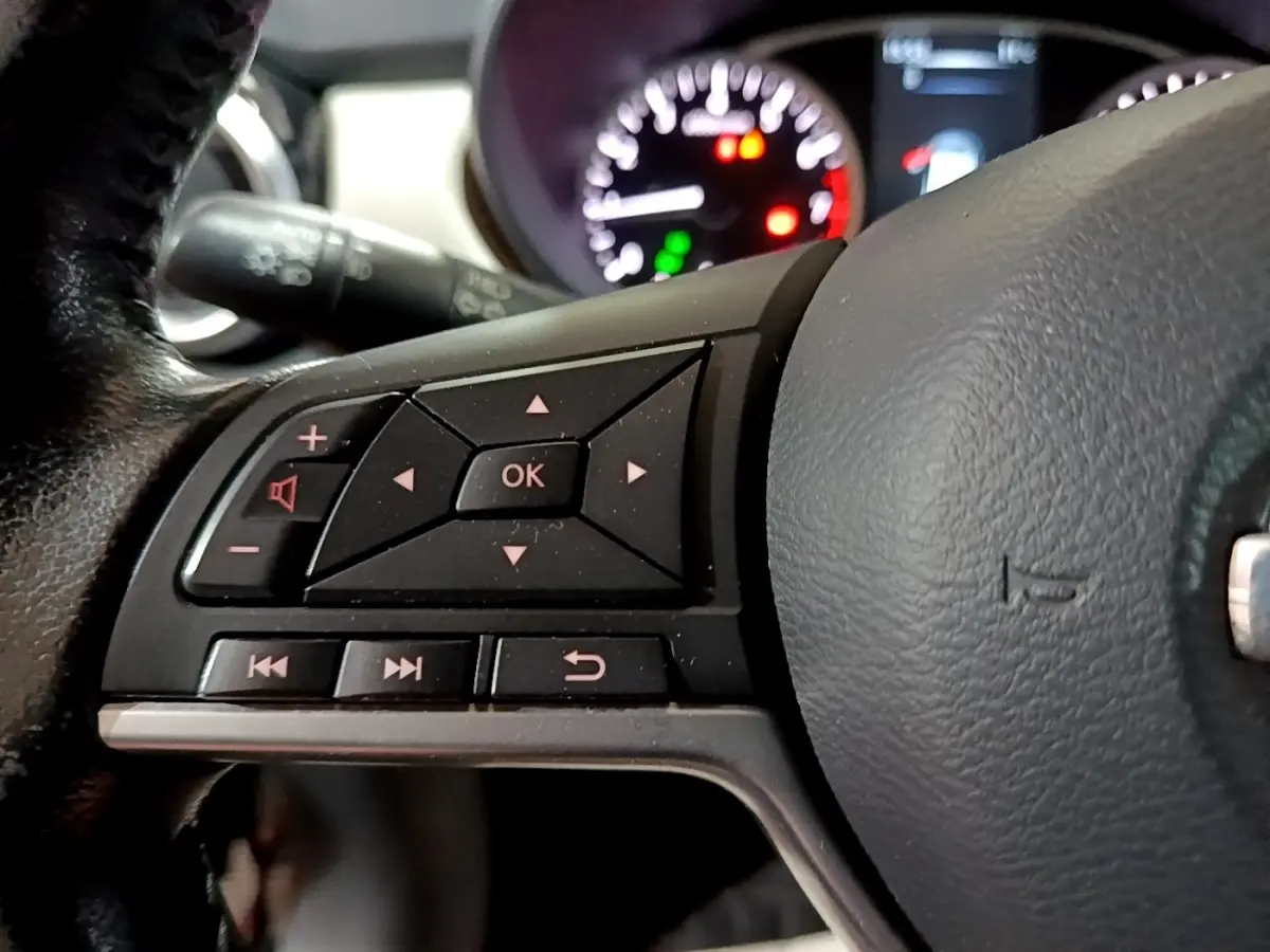 Gros plan sur le volant cuir noir de la Nissan Micra 2017, avec commandes multifonctions et tableau de bord flou en arrière-plan.