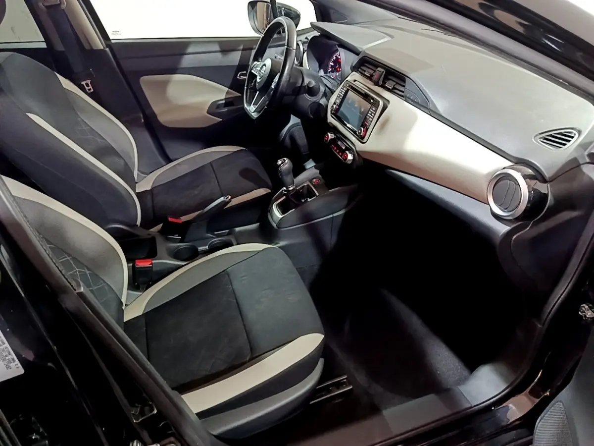 Vue intérieure côté conducteur de la Nissan Micra IG-T 90 N-Connecta noire, avec tableau de bord clair et volant cuir multifonctions.