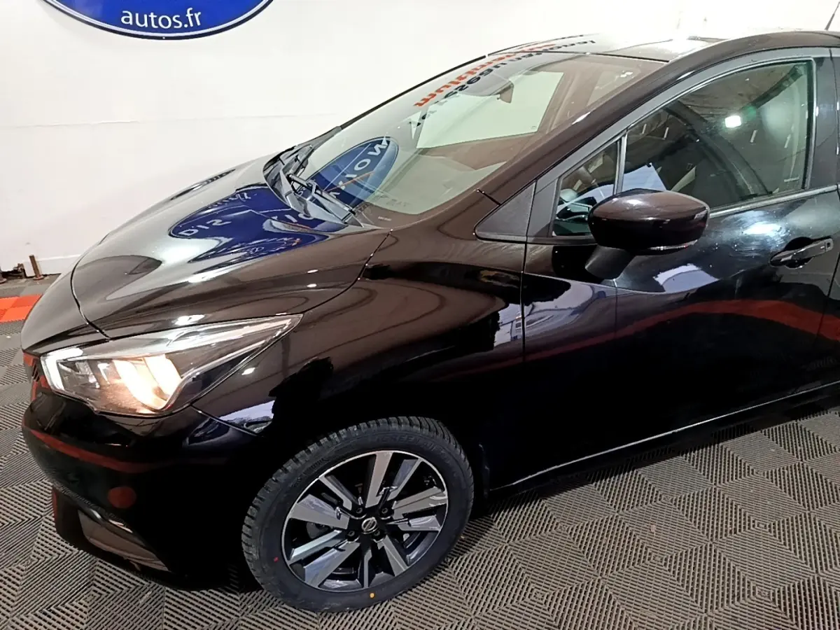 Vue 3/4 avant droit d'une Nissan Micra IG-T 90 N-Connecta noire, avec phares allumés et jantes alliage distinctives.