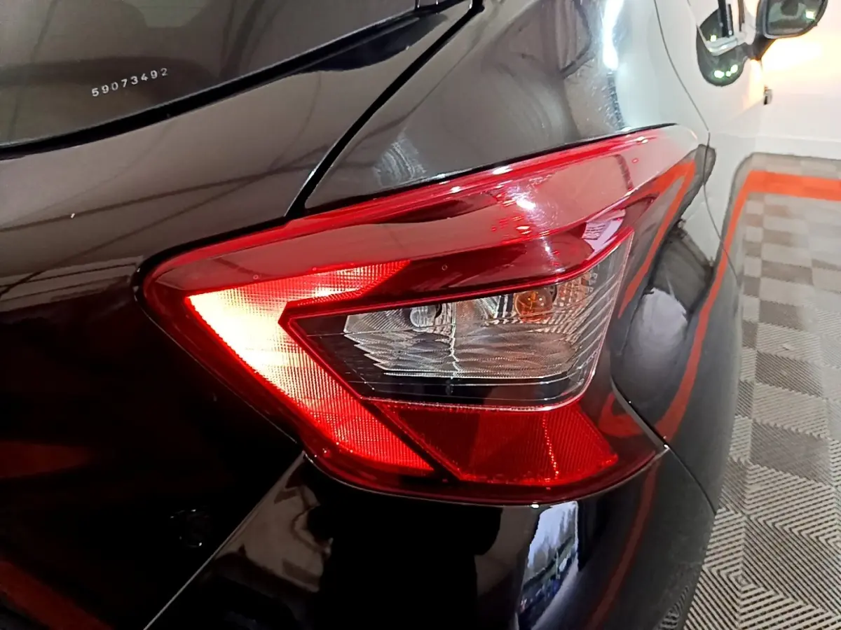 Gros plan sur le feu arrière droit rouge d’une Nissan Micra IG-T 90 N-Connecta noire, avec reflet sur la carrosserie brillante.