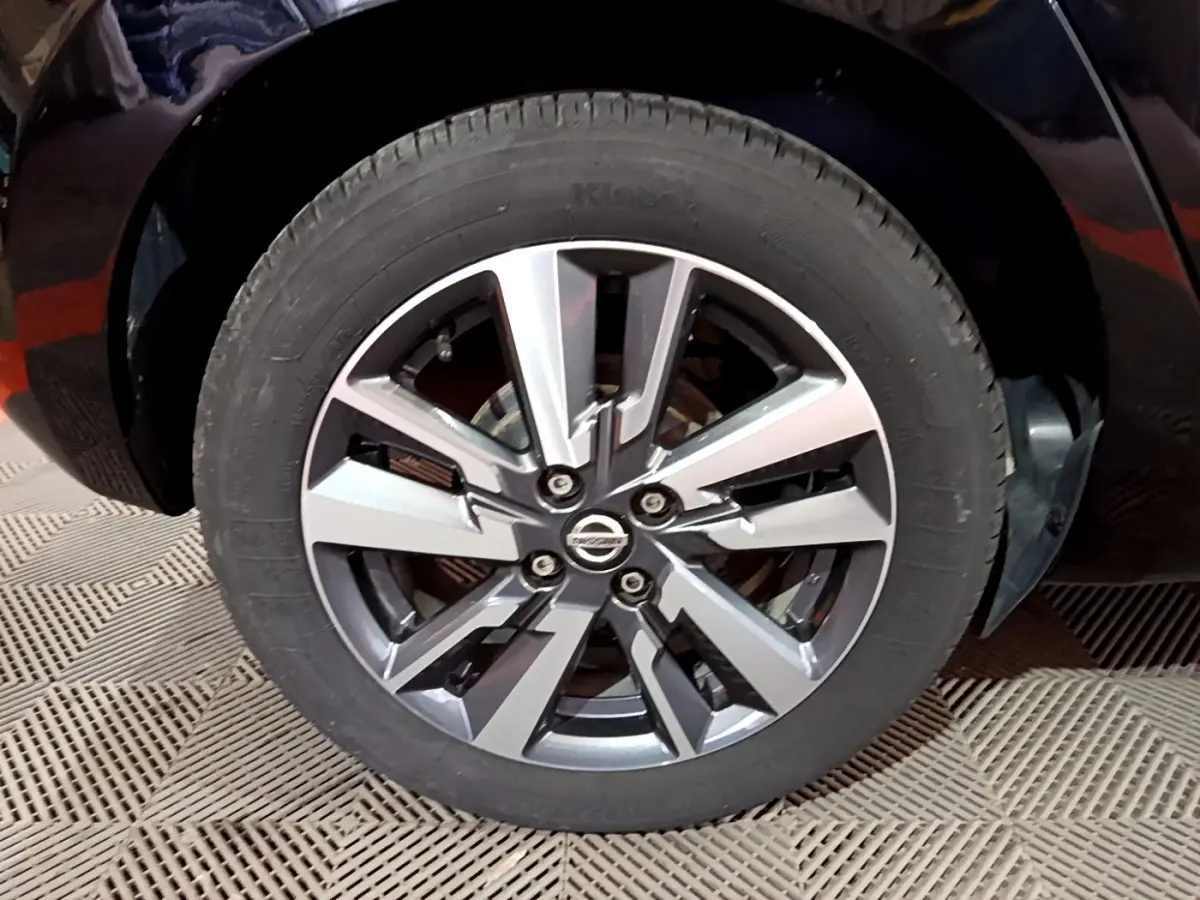 Gros plan sur la roue avant droite d’une Nissan Micra noire, mettant en valeur la jante alliage au design moderne.