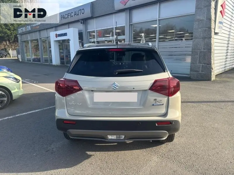 Vue arrière d'un Suzuki Vitara 1.4 Boosterjet Hybrid blanc ivoire avec toit noir, garé devant un concessionnaire.