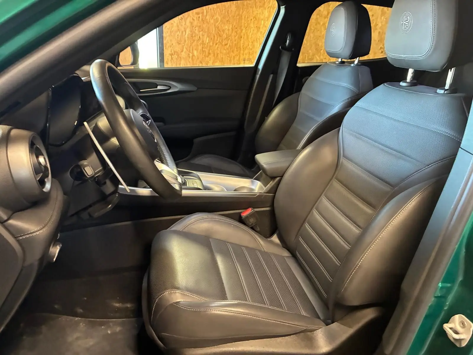 Vue intérieure côté conducteur de l'Alfa Romeo Tonale vert foncé, sièges en cuir noir avec logo Alfa Romeo brodé.
