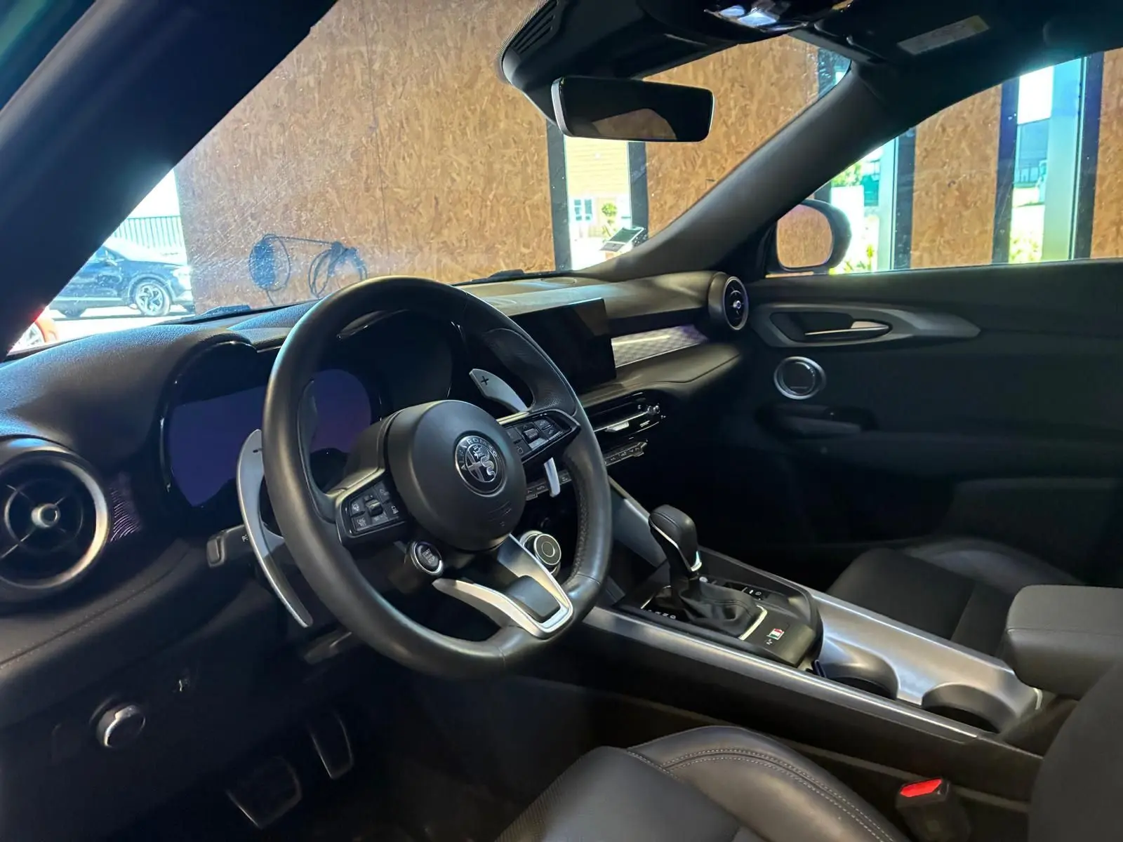 Vue intérieure côté conducteur de l'Alfa Romeo Tonale 1.5 MHEV 2022 avec tableau de bord noir et volant cuir.