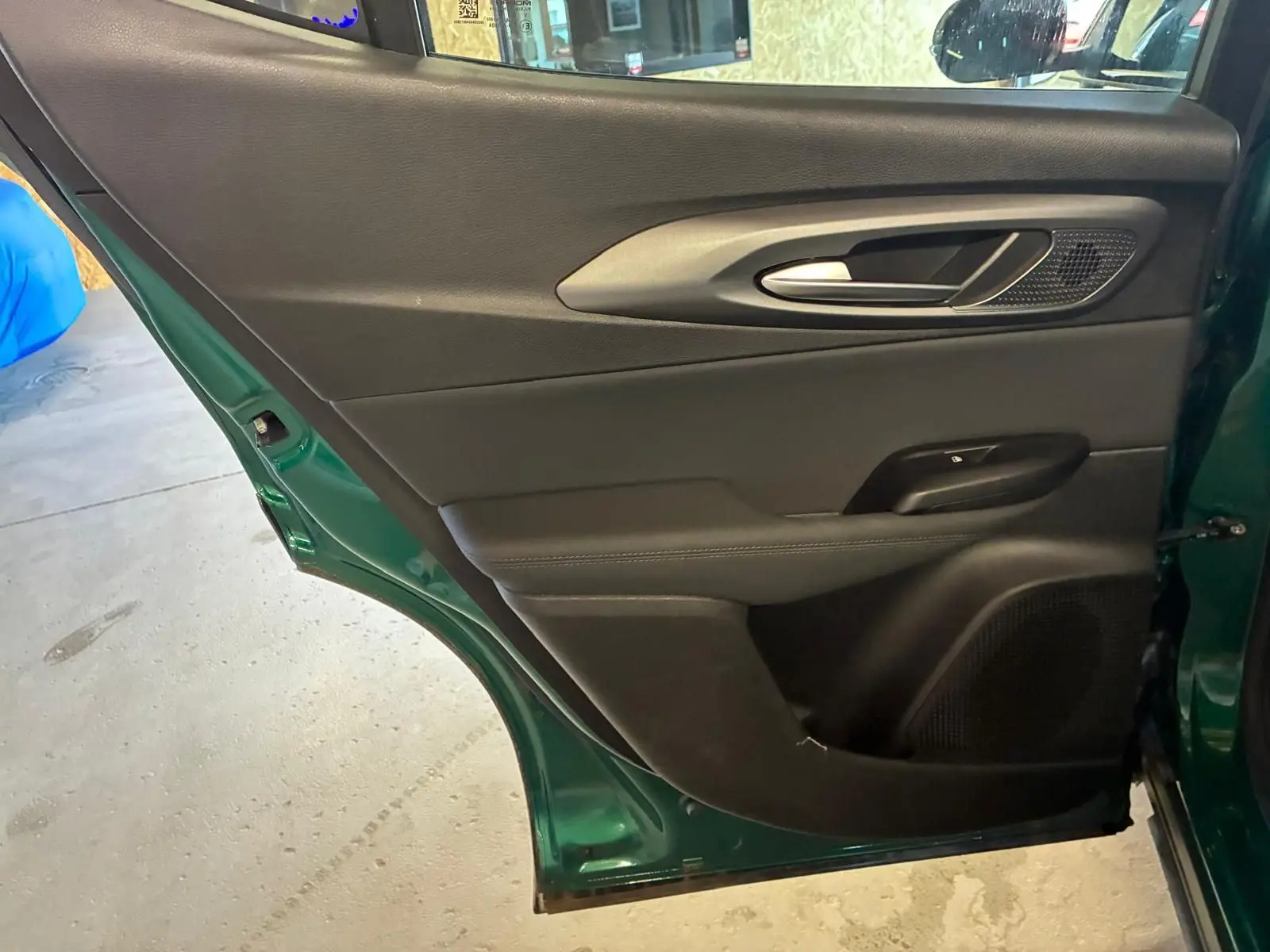 Vue intérieure côté gauche de la porte arrière d'une Alfa Romeo Tonale vert foncé, avec garniture noire et poignée argentée.