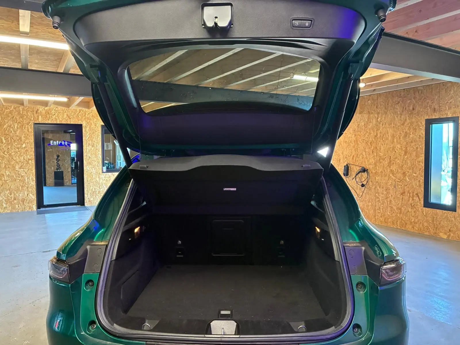 Coffre ouvert vu de l'arrière d'un Alfa Romeo Tonale vert foncé dans un garage avec intérieur noir visible.