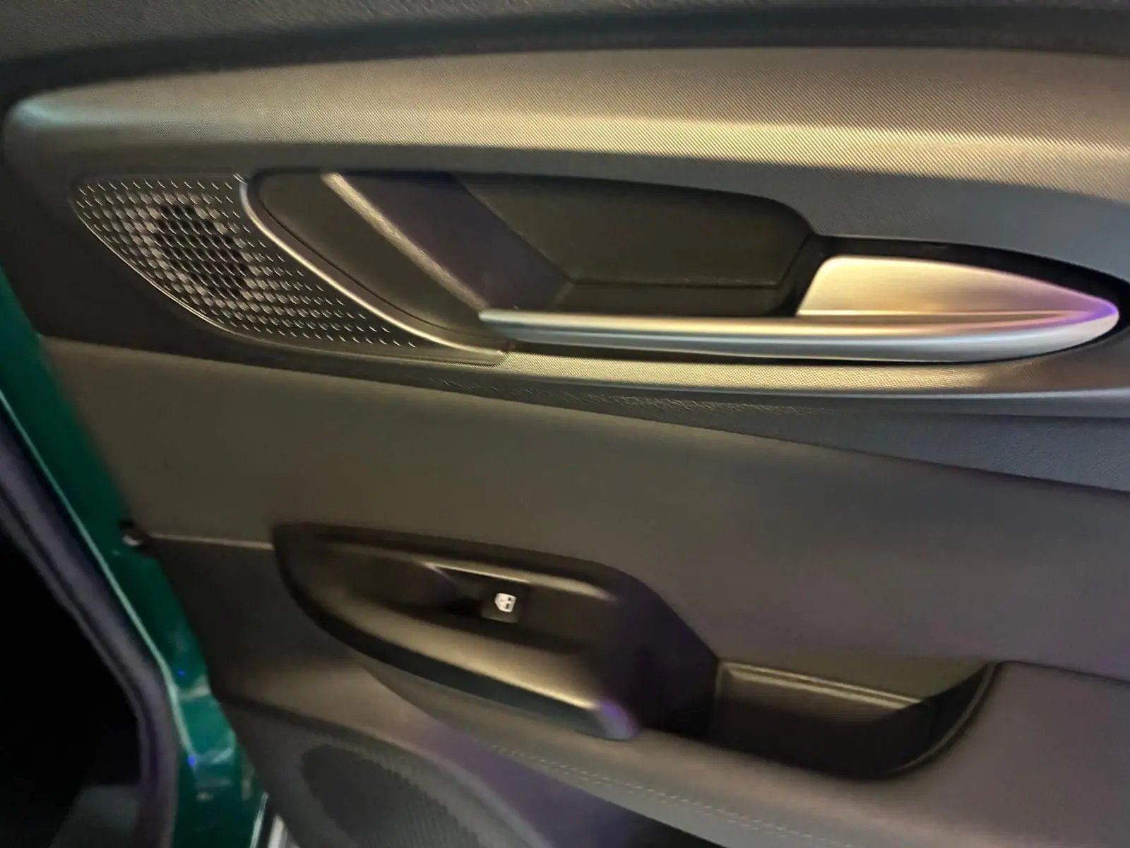 Gros plan sur la porte côté gauche d'une Alfa Romeo Tonale vert foncé, avec poignée argentée et commande de fenêtre.