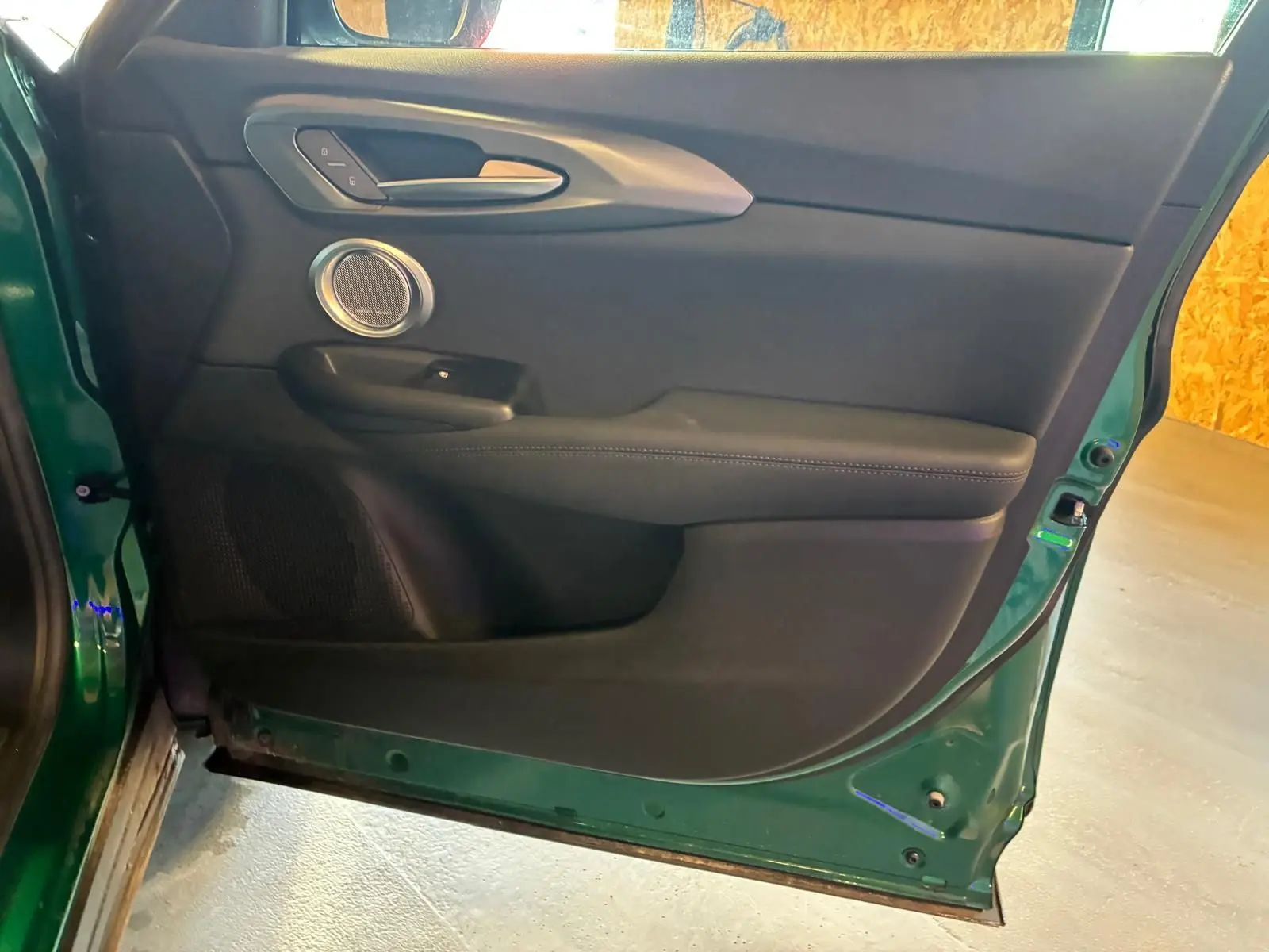 Vue intérieure de la porte avant gauche de l'Alfa Romeo Tonale vert foncé, avec garniture noire et haut-parleur rond.