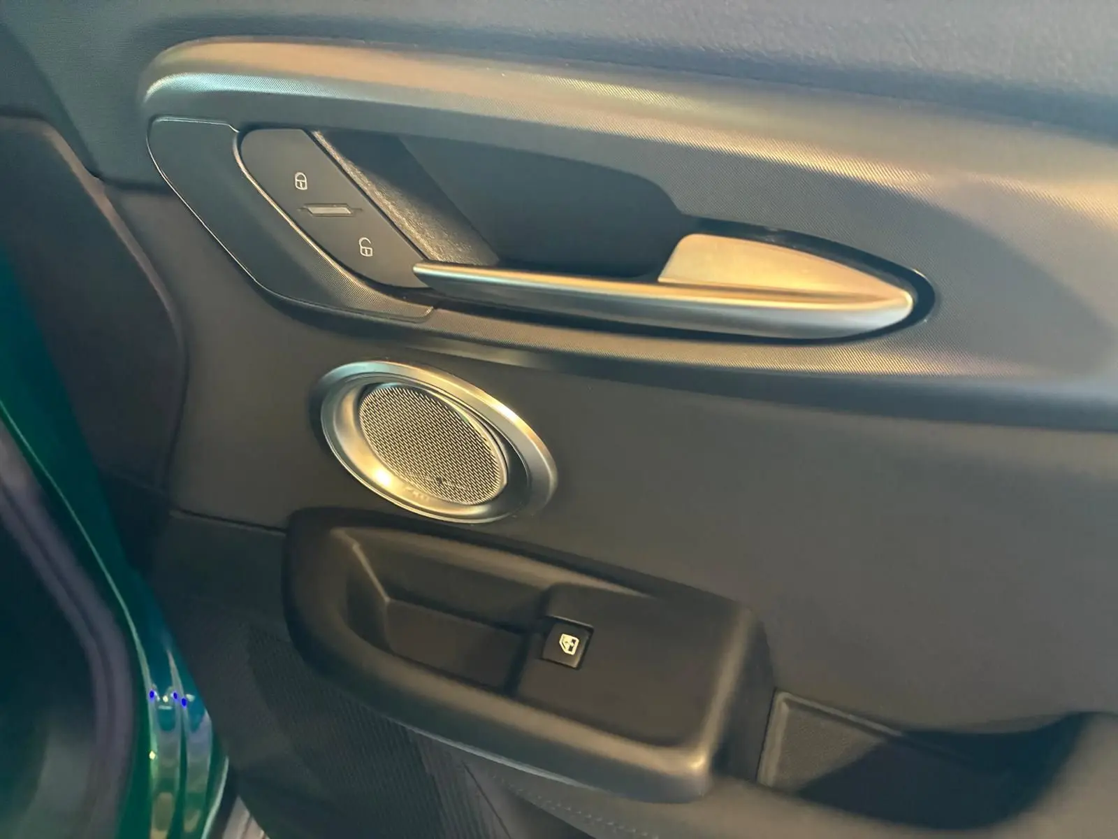 Détail de la porte côté gauche de l'Alfa Romeo Tonale vert foncé, avec poignée argentée et haut-parleur rond intégré.