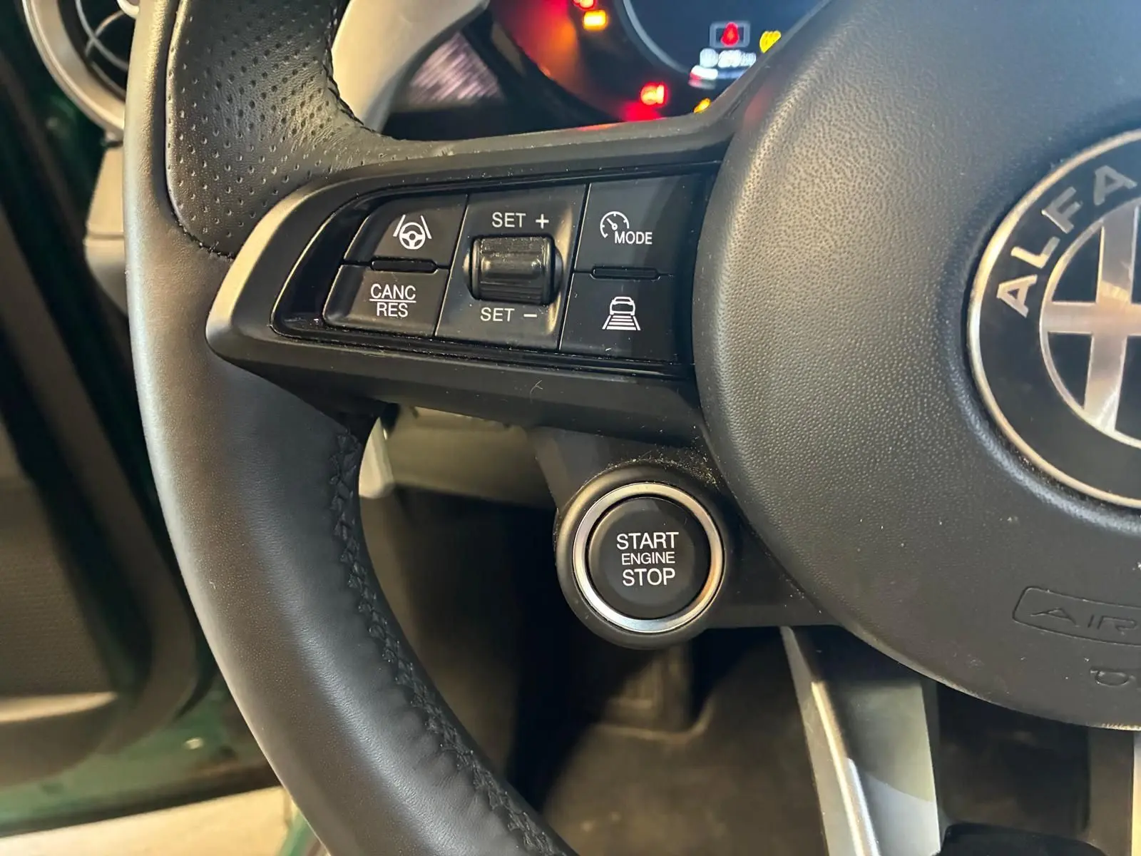 Gros plan sur le volant noir de l'Alfa Romeo Tonale avec boutons de régulateur et bouton start/stop visible.
