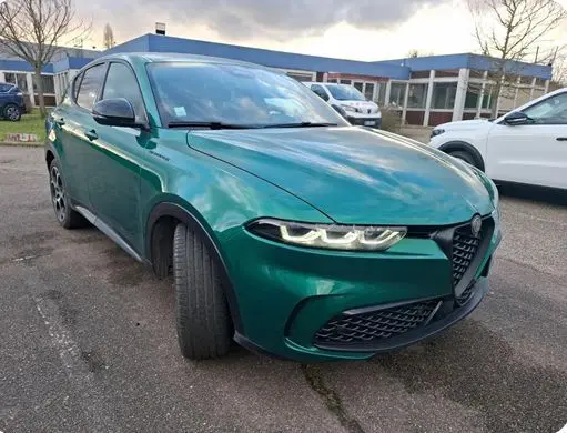 Vue de profil côté gauche d'une Alfa Romeo Tonale vert foncé avec jantes sport et freins rouges, stationnée en intérieur.