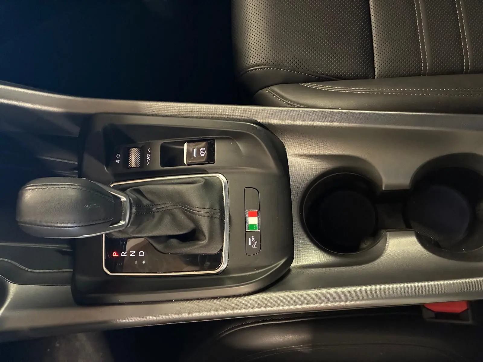 Gros plan sur la console centrale noire de l'Alfa Romeo Tonale avec levier de vitesse automatique et drapeau italien.