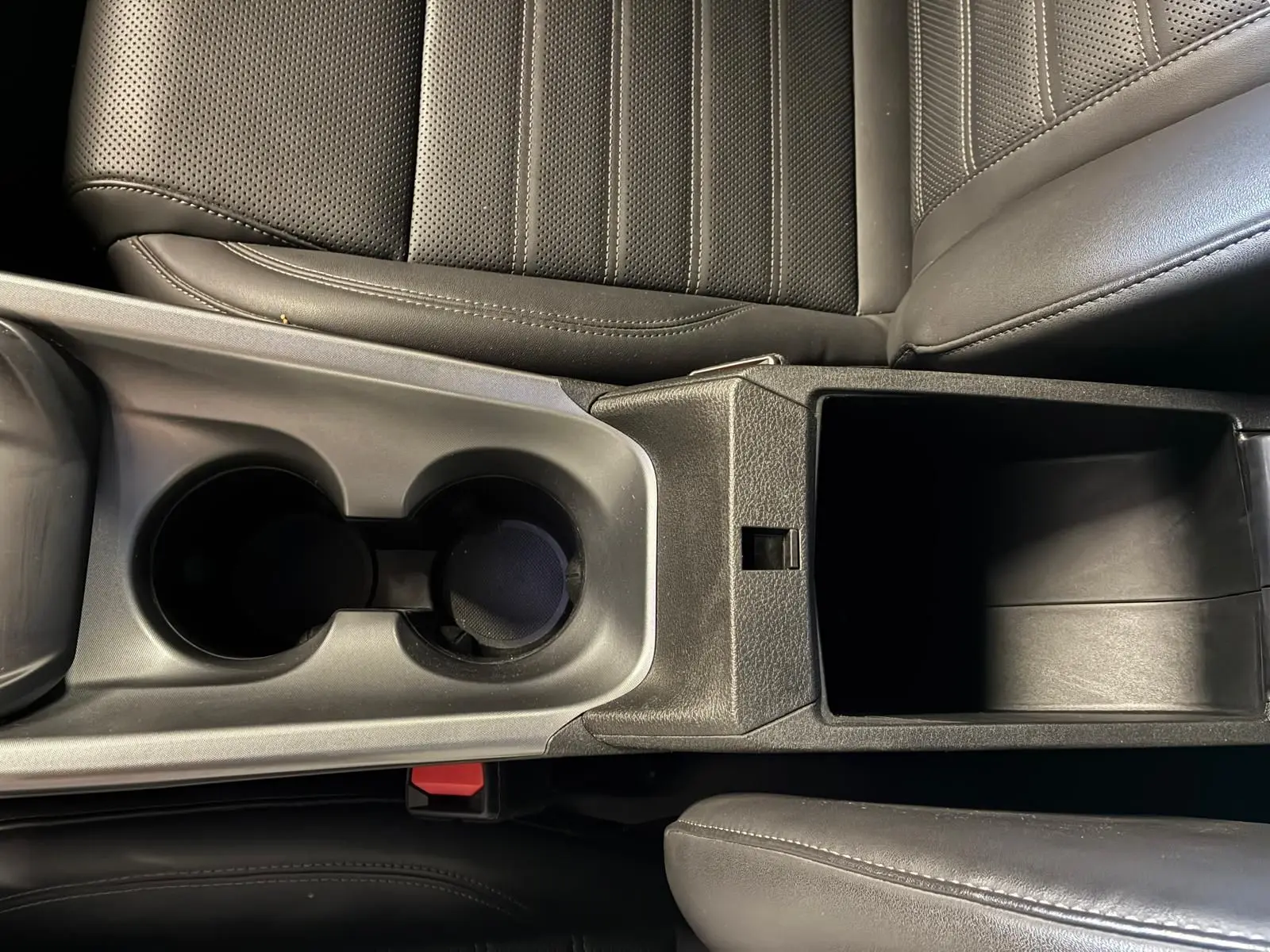 Vue en plongée sur la console centrale en cuir noir de l'Alfa Romeo Tonale 2022, avec porte-gobelets et rangement ouvert.