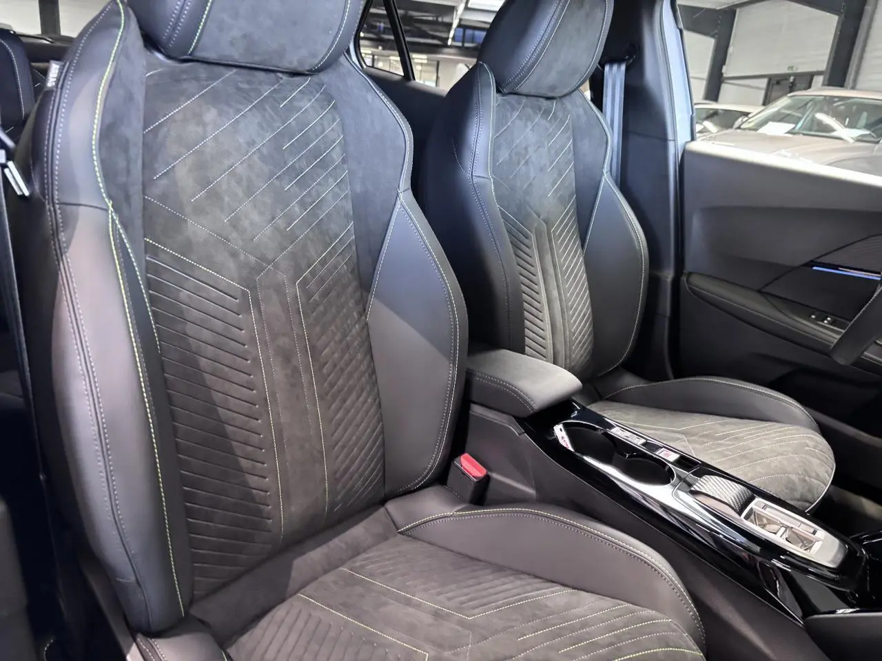 Vue intérieure rapprochée des sièges avant en Alcantara noir avec surpiqûres vertes et console centrale brillante.