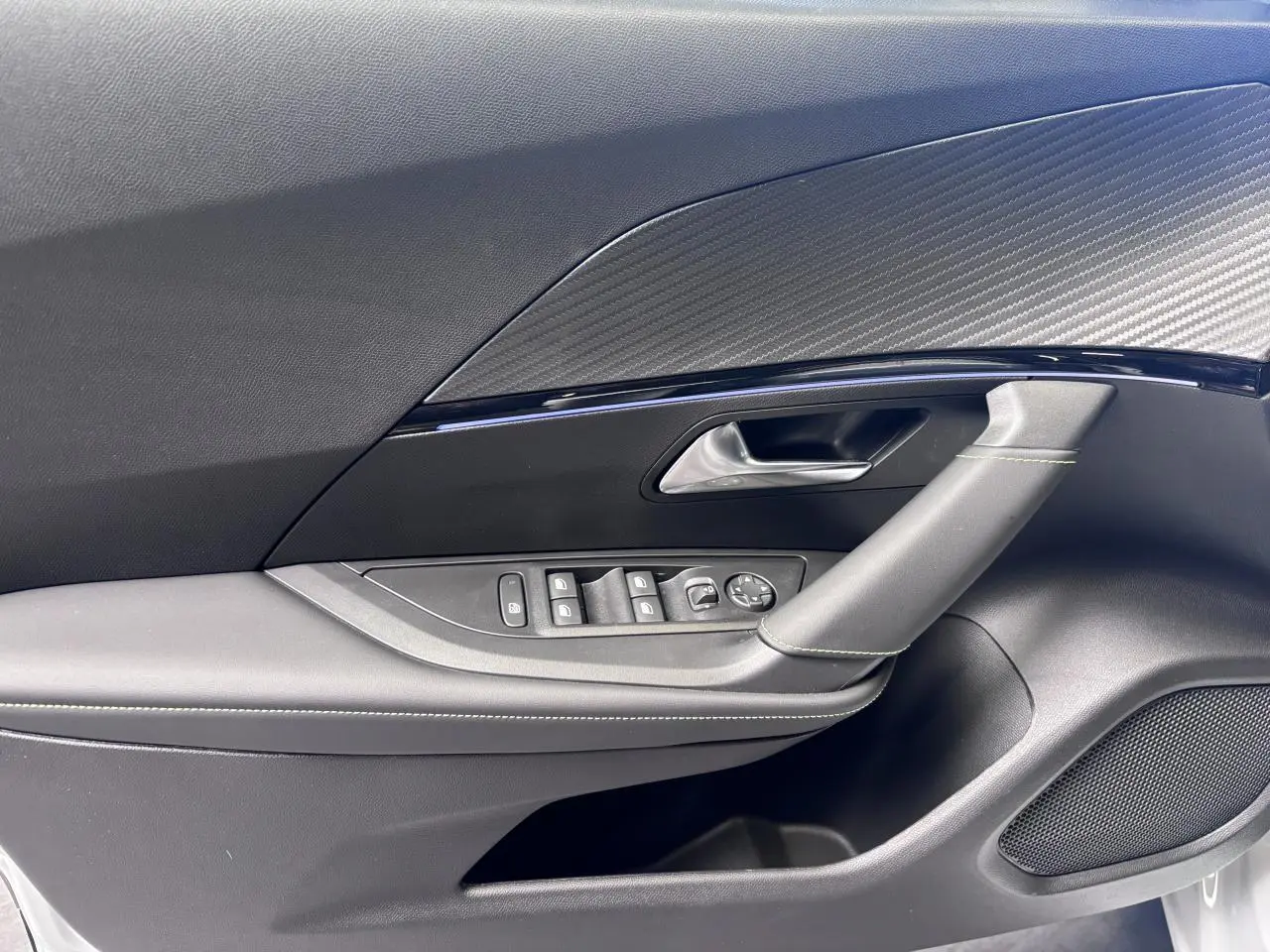 Détail de la porte avant gauche du Peugeot 2008 2026, avec commandes de vitres et insert décor carbone.