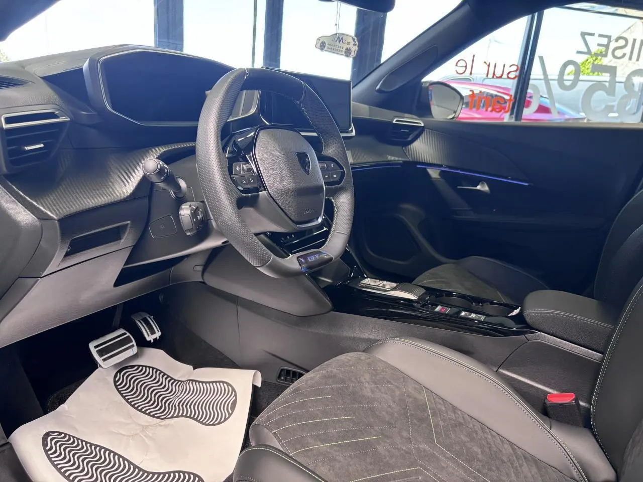 Vue intérieure côté conducteur du Peugeot 2008 1.2i Hybrid 2026, avec volant compact, sellerie Alcantara noire et surpiqûres vertes.