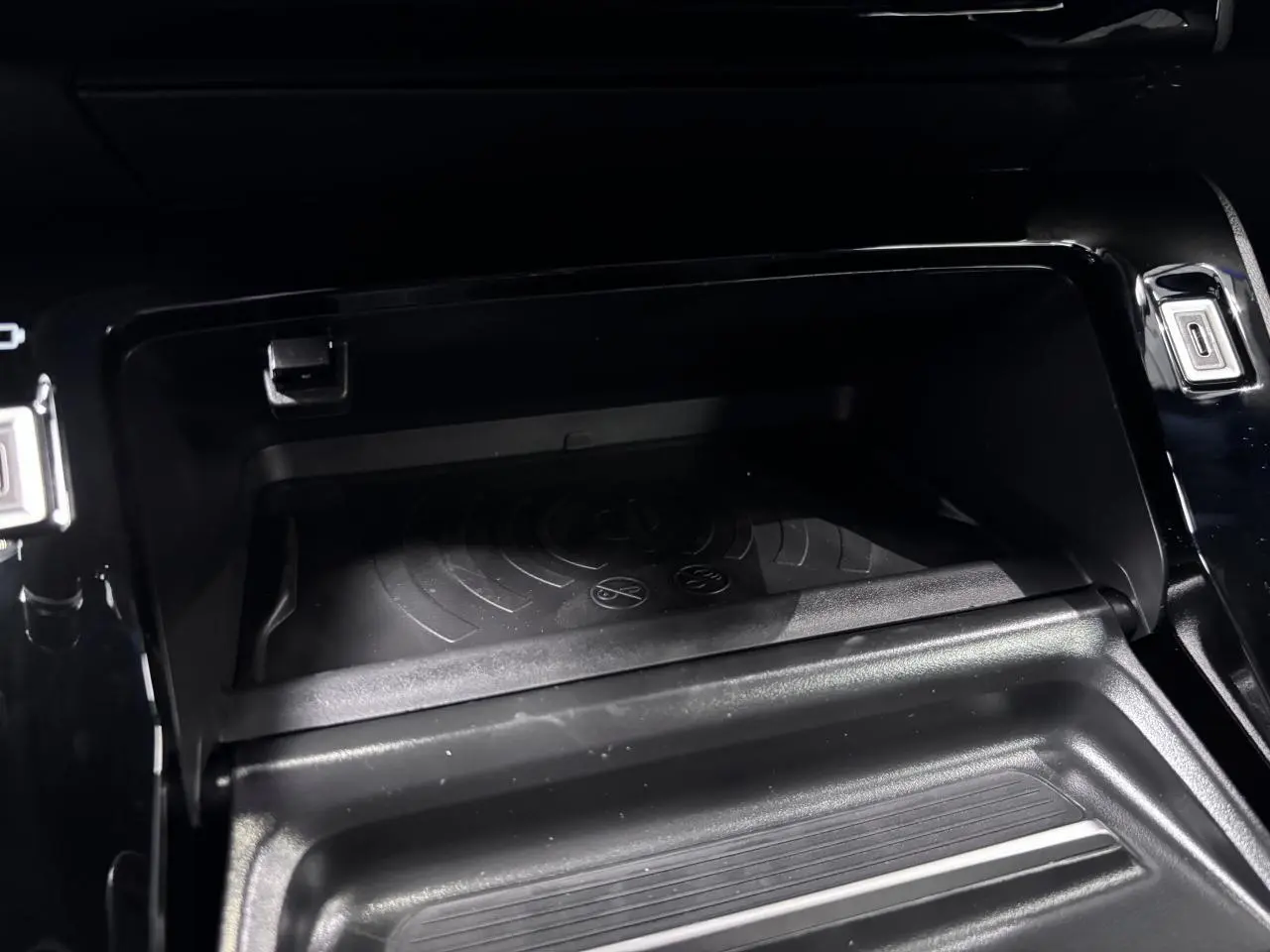 Vue rapprochée de la console centrale noire du Peugeot 2008 1.2i Hybrid avec chargeur smartphone sans fil intégré.