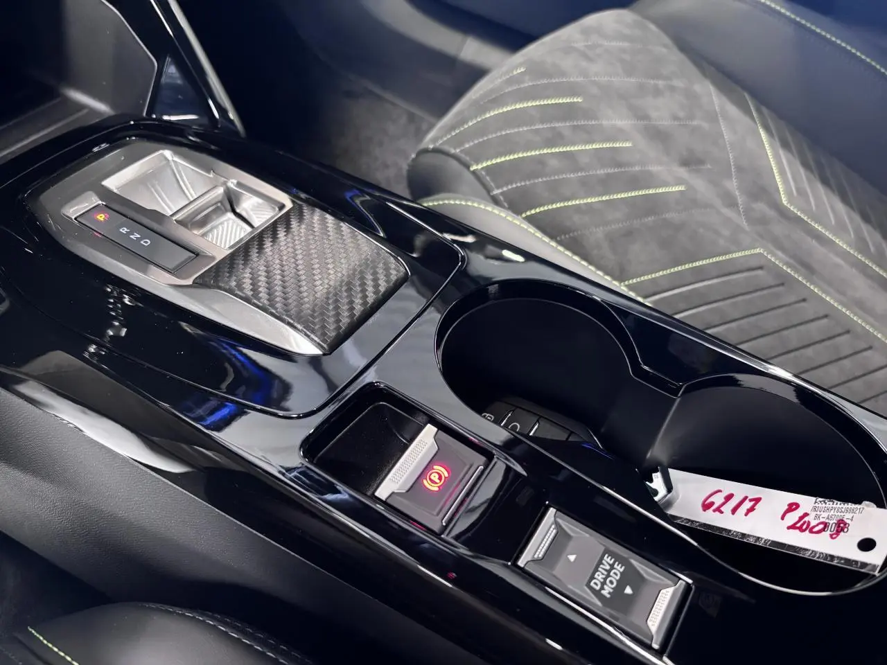 Vue rapprochée de la console centrale noire brillante avec levier de vitesses et sièges Alcantara noir surpiqués vert Adamite.