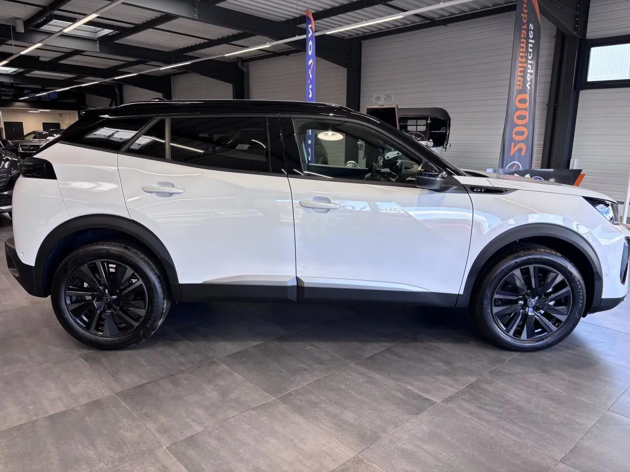 Peugeot 2008 1.2i Hybrid GT vue profil côté gauche, carrosserie blanche et toit noir avec jantes alliage noires.