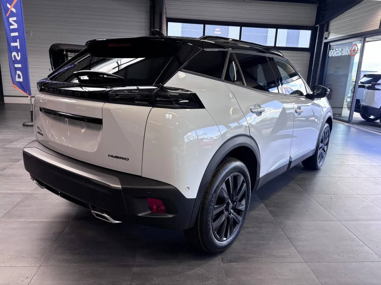 Vue 3/4 arrière droite du Peugeot 2008 hybride 2026 blanc avec toit noir et jantes alliage noires en showroom.