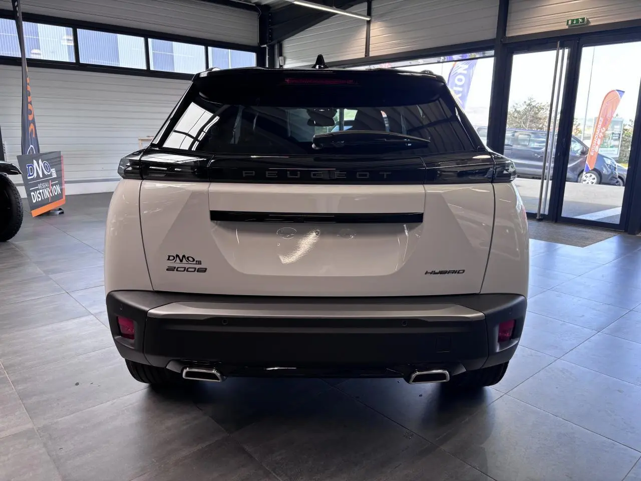 Vue arrière du Peugeot 2008 hybride blanc avec toit noir et double sortie d’échappement chromée en showroom.