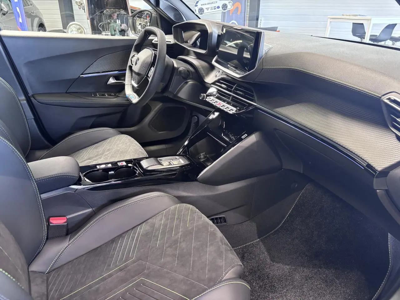 Intérieur avant droit du Peugeot 2008 1.2i Hybrid 2026 avec sellerie Alcantara noire et surpiqûres vertes, tableau de bord moderne.