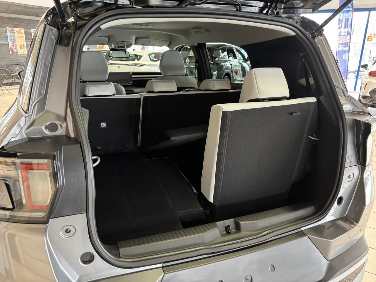 Vue arrière du coffre ouvert du Citroën C3 Aircross gris, montrant la banquette 7 places avec siège arrière partiellement relevé.