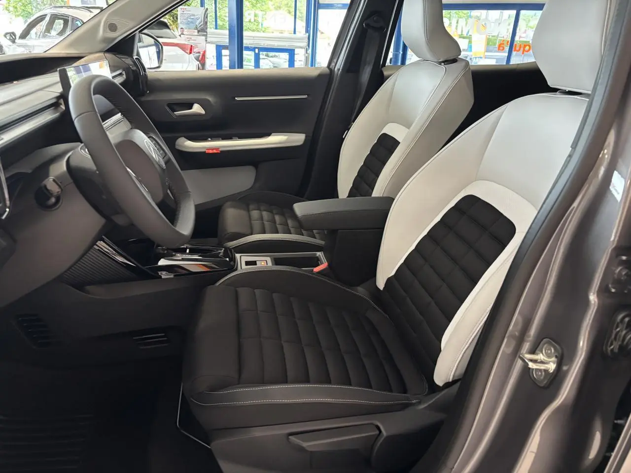Vue intérieure côté conducteur du Citroën C3 Aircross 2026 gris, sièges bicolores noir et blanc avec accoudoir central.