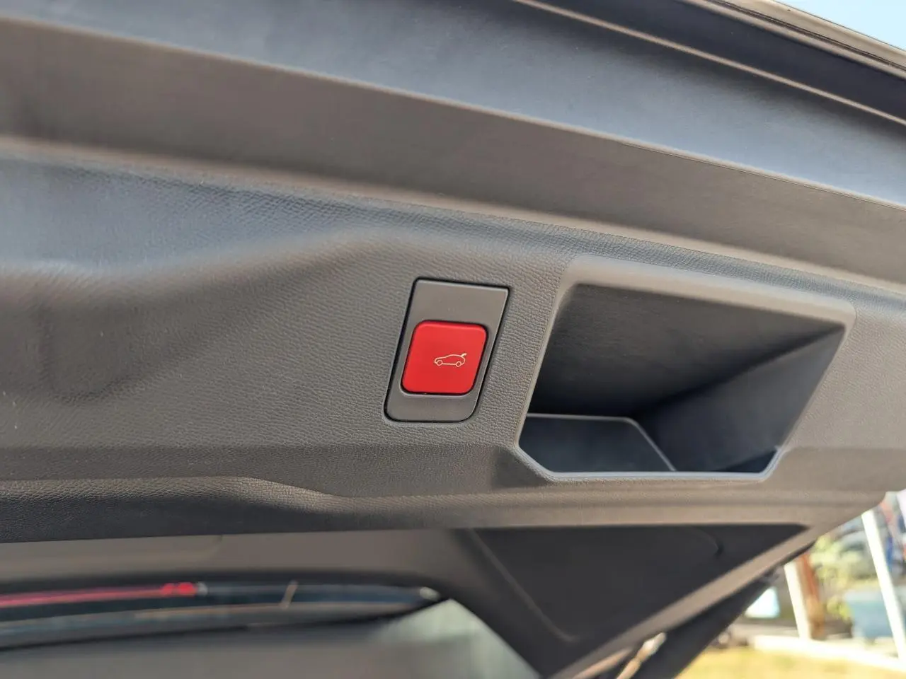 Bouton rouge d'ouverture électrique du hayon sur le panneau intérieur du coffre d'un Peugeot 5008 blanc.