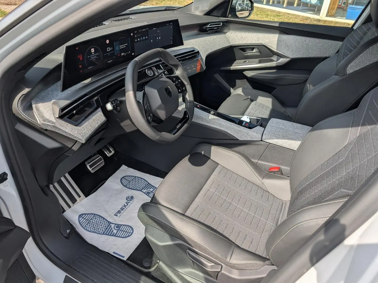 Vue intérieure côté conducteur du Peugeot 5008 blanc 2025, montrant le volant compact et l'écran panoramique incurvé.