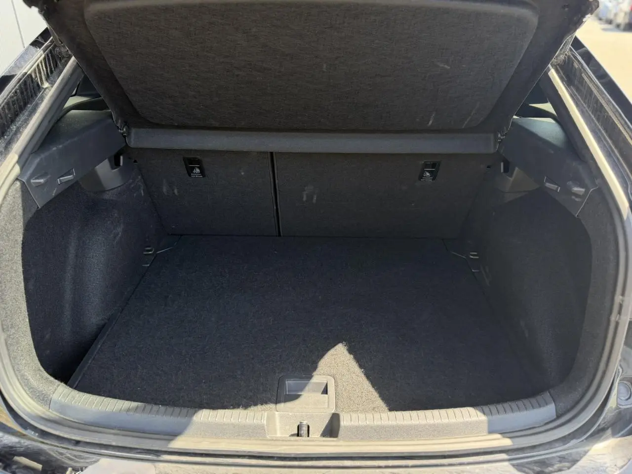 Coffre ouvert vu de l'arrière d'un Volkswagen Taigo noir, espace de chargement propre et vide.
