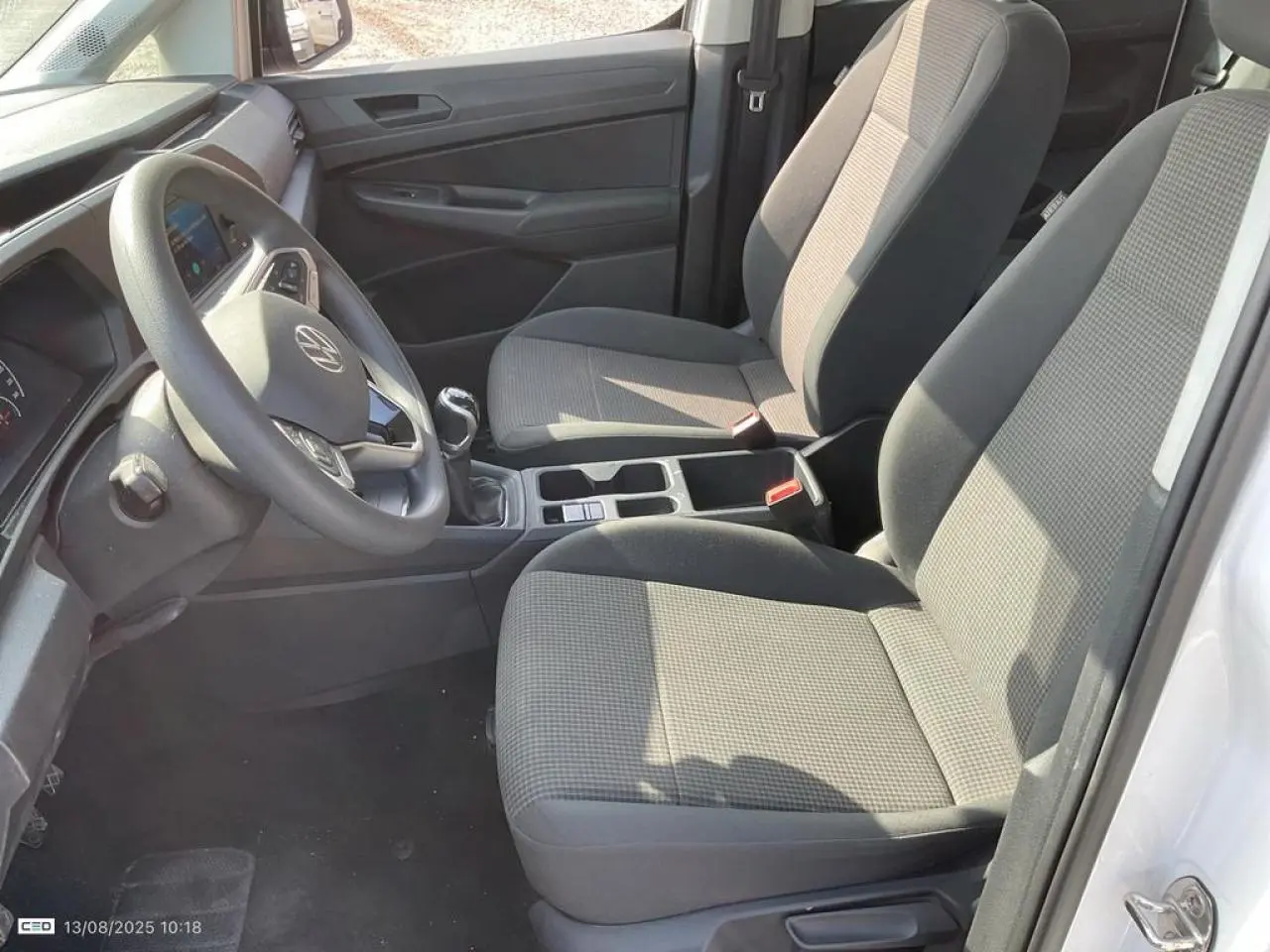 Vue intérieure côté conducteur du Volkswagen Caddy blanc Candy 2024 avec sièges tissu gris et volant multifonctions.