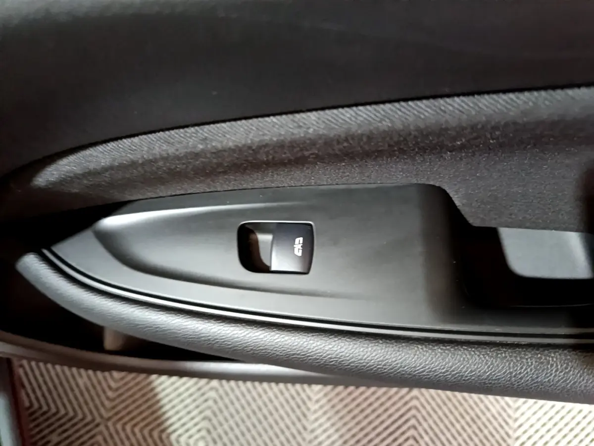 Gros plan sur le bouton de verrouillage centralisé noir sur la porte intérieure côté gauche de l’Opel Insignia rouge.