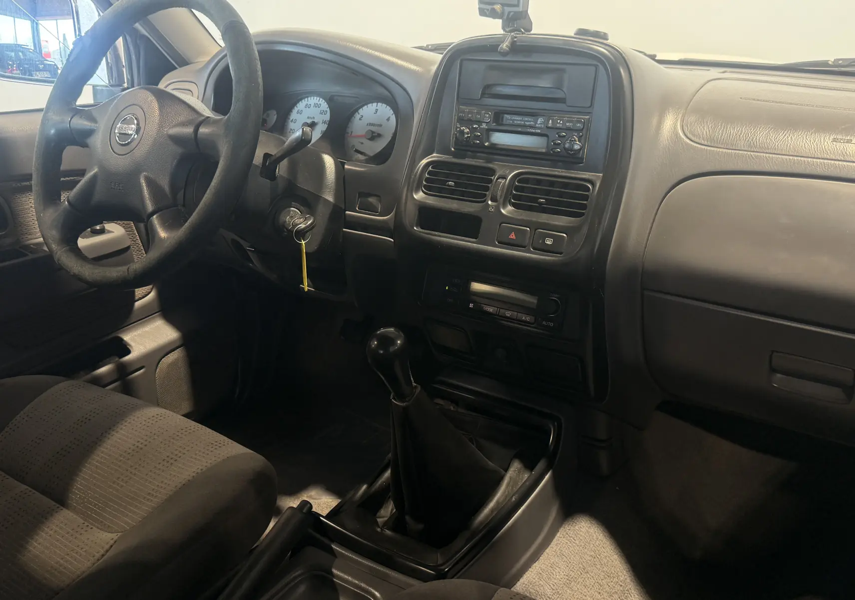 Vue intérieure côté conducteur du tableau de bord et levier de vitesse manuel du Nissan Navara NP300 blanc de 2002.