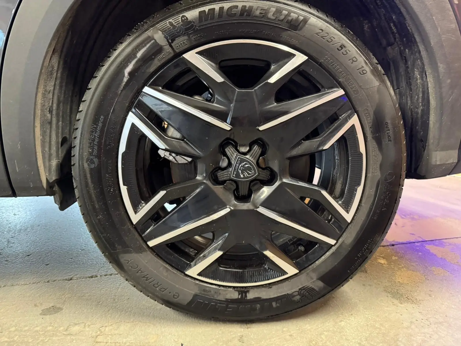 Gros plan sur la jante noire et argentée du Peugeot 5008 gris, mettant en valeur le logo lion au centre.