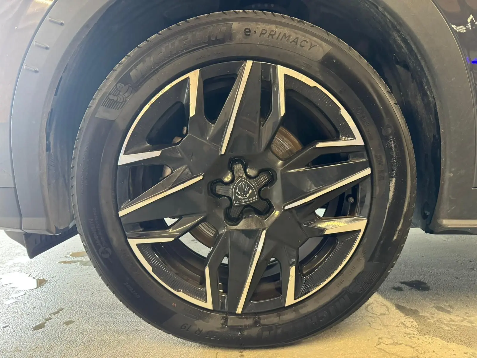 Gros plan sur la roue avant gauche du Peugeot 5008 gris 1.2 HYBRID 136 GT avec jante alliage noire et argent.